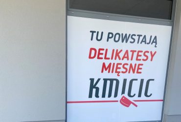 zdjęcie przedstawia witrynę lokalu usługowego z napisem: Tu powstają Delikatesy Mięsne Kmicic. Sklep mięsny na Chwarznie