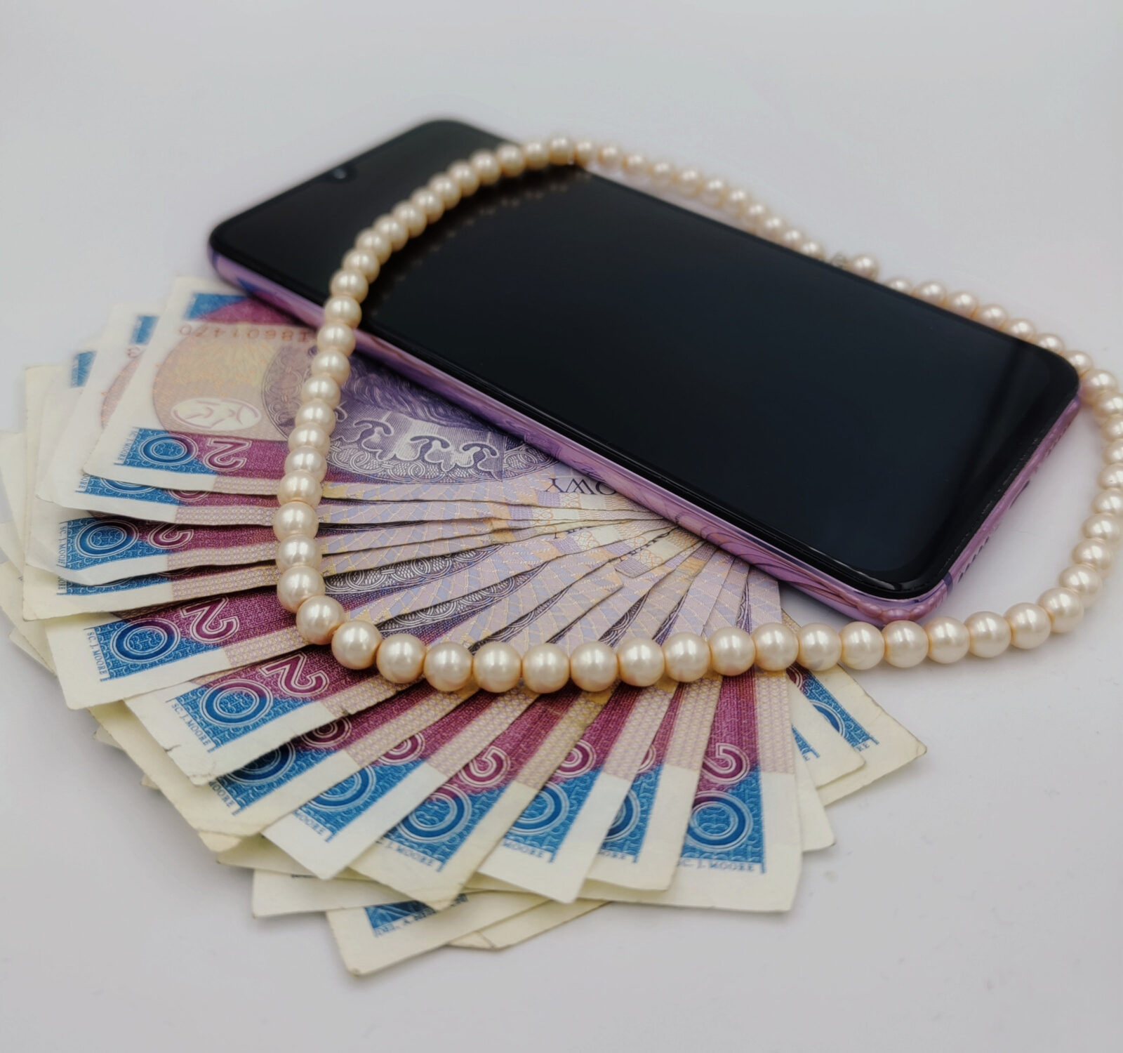 zdjęcie ilustracyjne, na którym widać banknoty o wartości 20 zł, korale oraz smartfon w fioletowej obudowie. Autorem zdjęcia jest Agnieszka Rodziewicz.