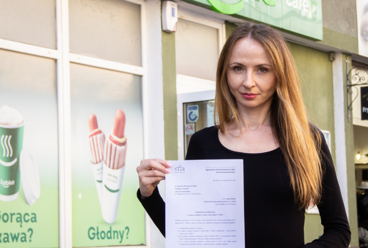 Zdjęcie przedstawia Agnieszka Dziemianowicz-Bąk z pismem z zapytaniem otwartym do Powiatowego Urzędu Pracy w Gdyni. Posłanka stoi obok sklepu sieci Żabka Polska.