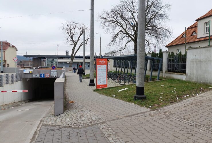 Zdjęcie przedstawia Węzeł Integracyjny w Chyloni. Widać na nim wejście do parkingu podziemnego oraz stację MEVO. Zdjęcie wykonano 13.03.2024 r.